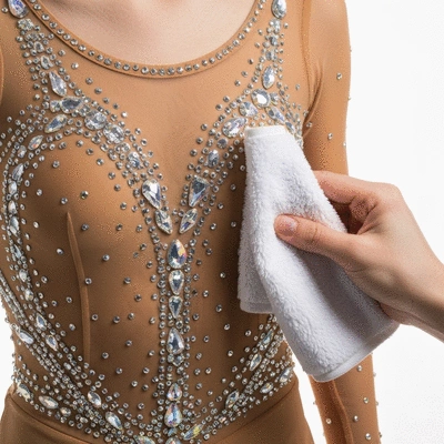 Figure skating dress with sparkling rhinestones being carefully inspected and cleaned with a soft cloth